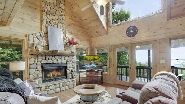 A cozy cabin interior with a stone fireplace, leather sofas, and a large TV screen. - Stunning Mountain Cabin w/ Hot Tub & Decks (Blue Ridge)