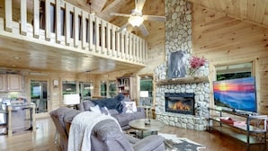 A spacious living room with a stone fireplace, a large television, and a cozy seating area. - Stunning Mountain Cabin w/ Hot Tub & Decks (Blue Ridge)