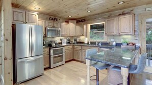 A modern kitchen with wooden cabinets, stainless steel appliances, and a central island with bar stools. - Stunning Mountain Cabin w/ Hot Tub & Decks (Blue Ridge)
