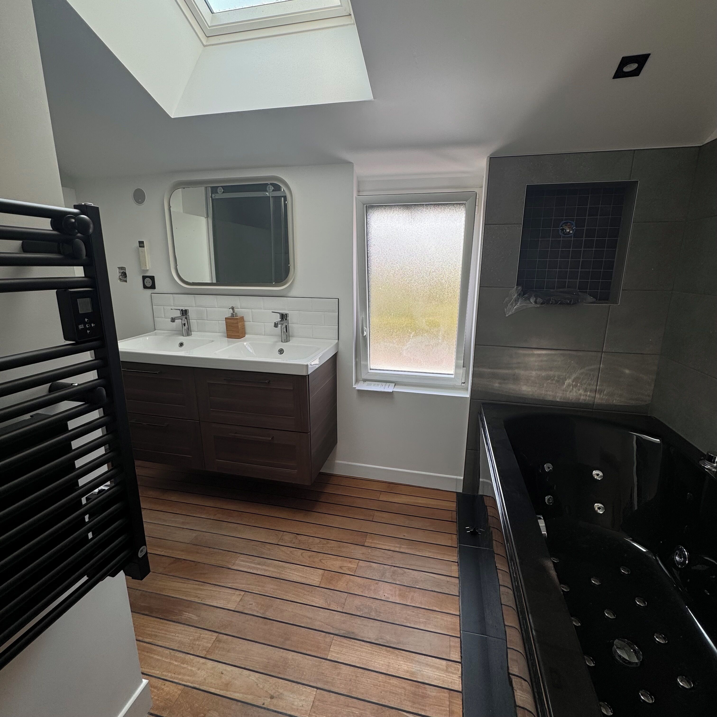 Une salle de bain moderne dotée d’un puits de lumière, d’un meuble-lavabo à deux vasques, d’une baignoire et d’une fenêtre.