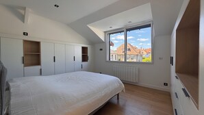A bedroom with a large bed, built-in wardrobes, a skylight, and a view of houses. - LePtiLoft Bayeux (Bayeux)