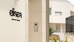 Ένα σύγχρονο κτίριο με μια επιγραφή που γράφει «elisea, η απόδρασή σας από την πόλη» και ένα σύστημα πρόσβασης με πληκτρολόγιο.
