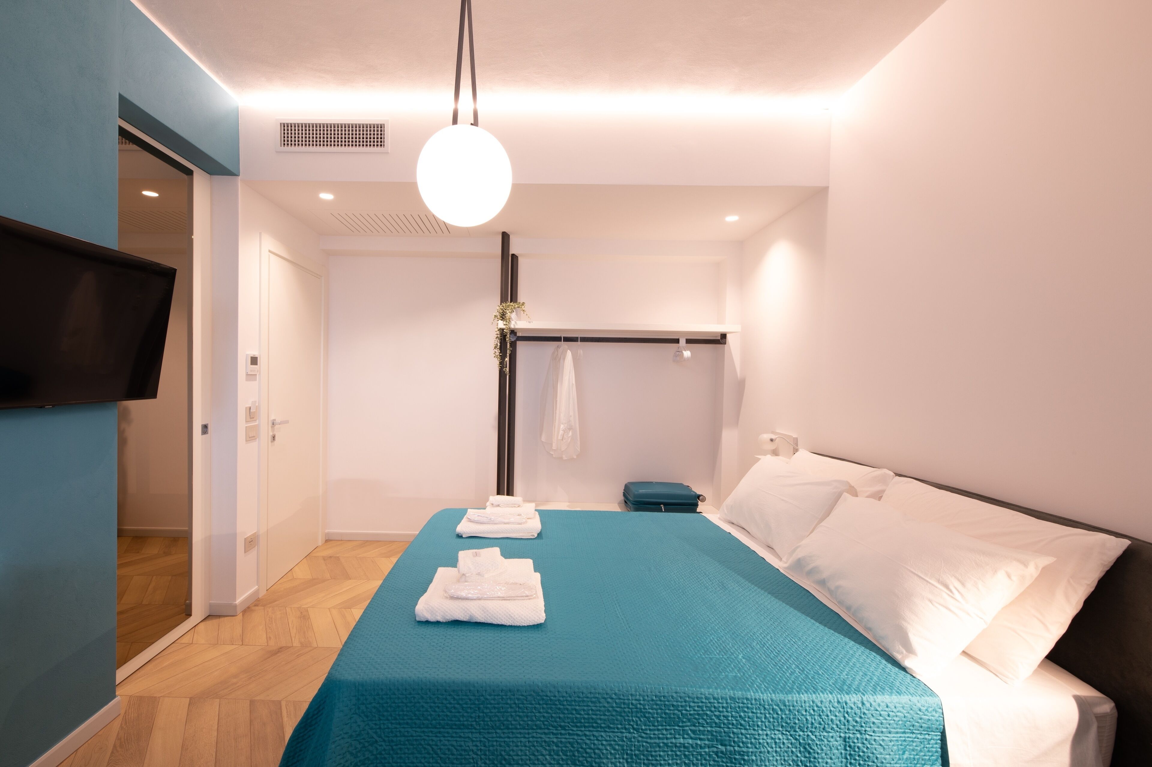 Une chambre d’hôtel moderne, équipée d’un lit, d’une télévision, d’une armoire et d’une salle de bain visible à travers une porte ouverte.