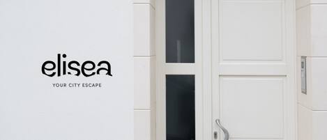 A white door with a glass panel and a keypad lock, set in a white building with a tiled floor.