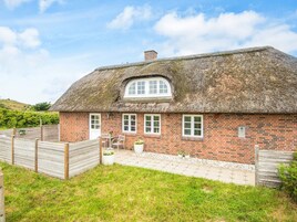 En bindingsværkshytte med murstensfacade, en lille veranda med et bord og stole, og en indhegnet have.