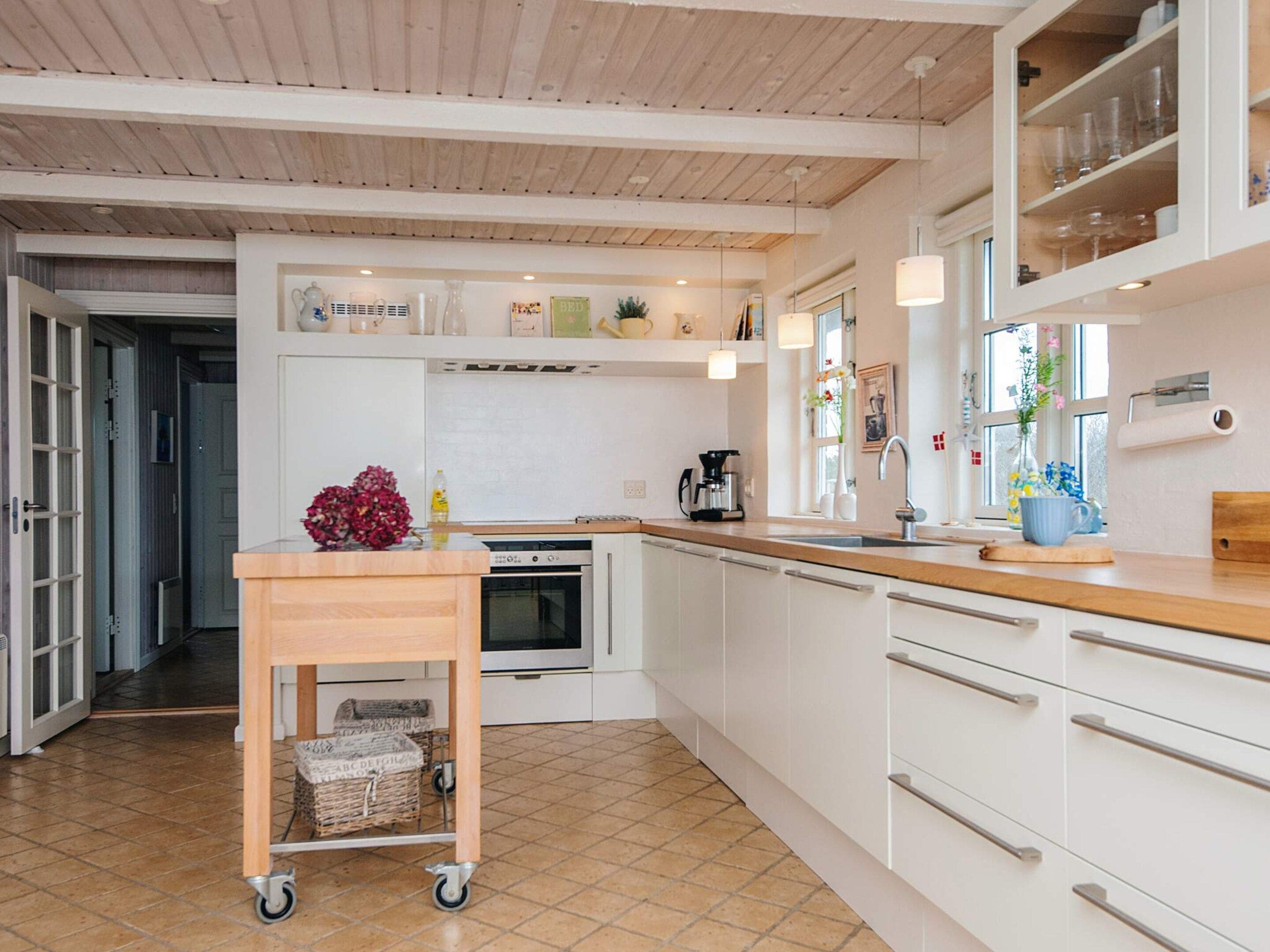 Une cuisine moderne avec des armoires blanches, un plan de travail en bois, un four encastré et un chariot muni de paniers.
