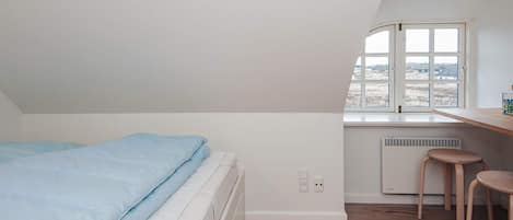 A bedroom with a bed, a window, a radiator, and a small stool.