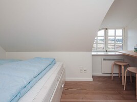 Un dormitorio con una cama, un ventanal, un radiador y un taburete pequeño.
