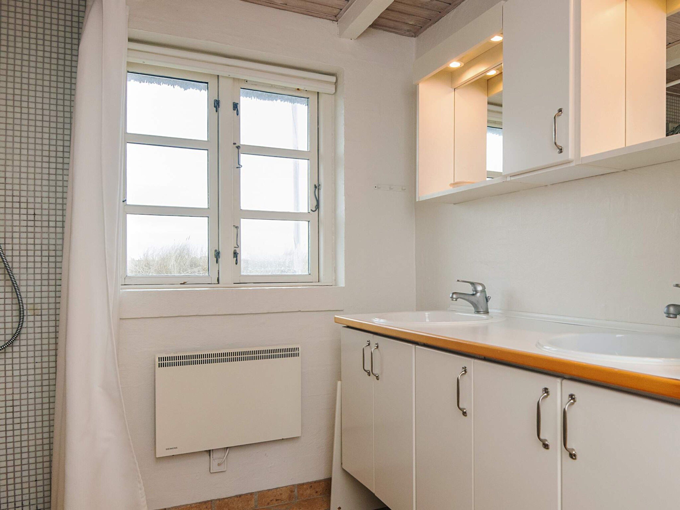A bathroom with a window, a sink, cabinets, and a radiator.