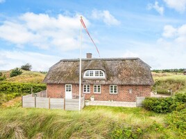 Una casa con techo de paja y fachada de ladrillo, un asta de bandera y un paisaje cubierto de césped.
