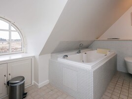 Un baño con una bañera grande, un inodoro y una ventana.