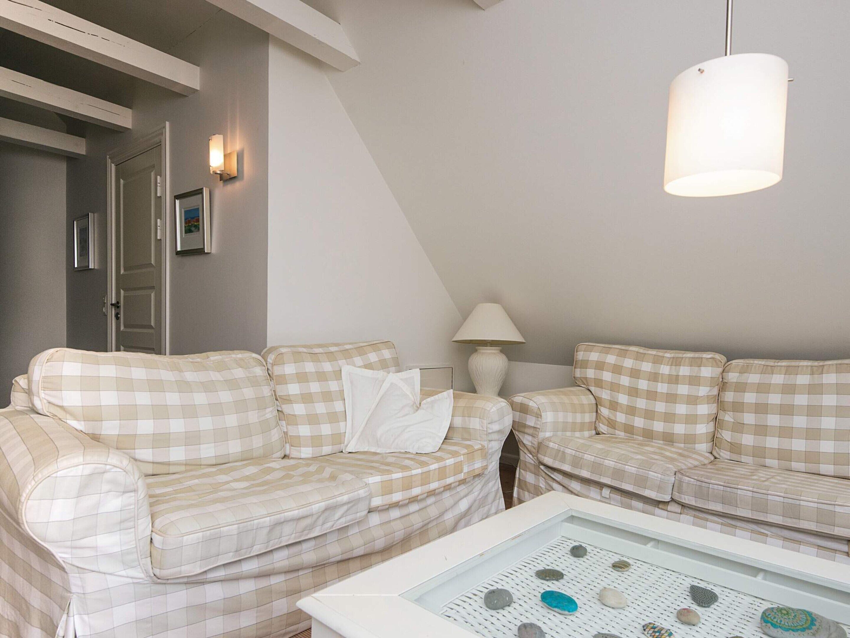 Un salon chaleureux avec deux canapés à carreaux, une table basse blanche ornée de pierres décoratives, une lampe et un luminaire au plafond.