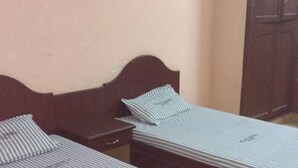 Dos camas individuales con ropa de cama a rayas en una habitación con cabecera de madera, una mesita de noche pequeña y un armario.