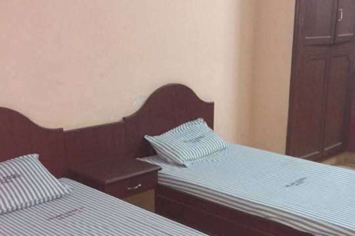Two single beds with striped bedding in a room with a wooden headboard, a small bedside table, and a cabinet.