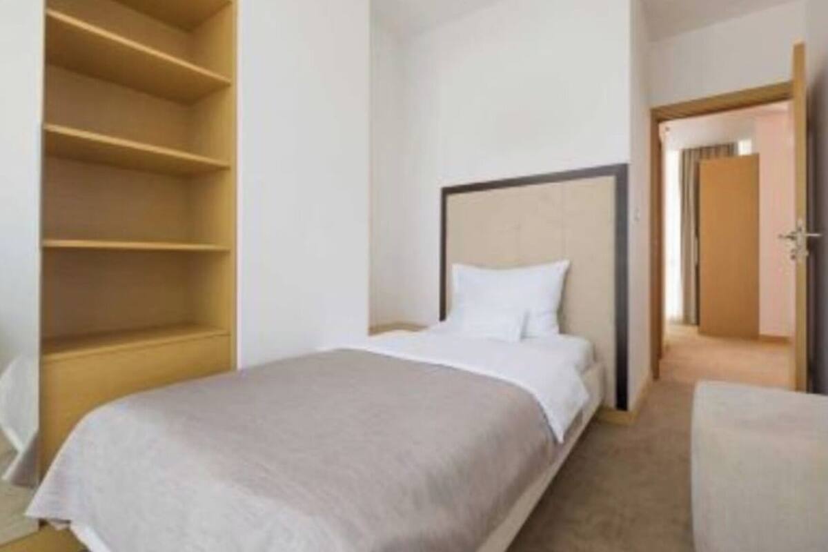 A hotel room with a bed, a wooden wardrobe, and a door leading to another room.