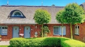 A traditional brick house with a thatched roof, two front doors, and a small garden with hedges. - Small break under thatch - quiet & cozy (Sankt Peter-Ording)