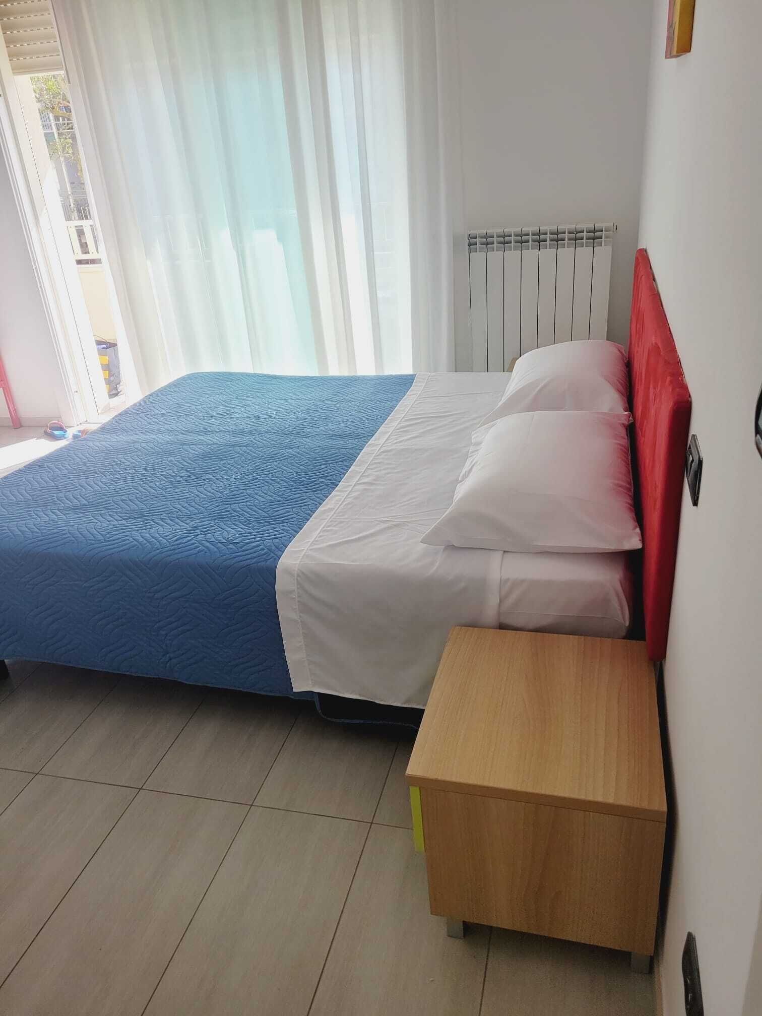 A hotel room with a bed, a bedside table, and a window with curtains.