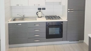 A compact kitchen with white and grey cabinetry, a stainless steel sink, a gas stove, and a built-in oven. - By the sea in Miramare di Rimini (Rimini)