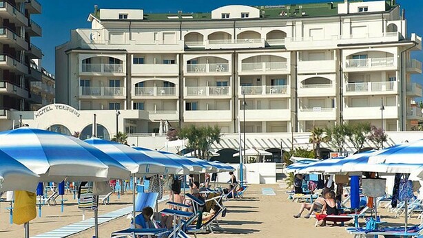 A hotel with multiple balconies, beach umbrellas, and beach chairs. - By the sea in Miramare di Rimini (Rimini)