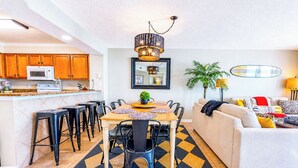 A modern kitchen with wooden cabinets, a microwave, and a dining area with a table and chairs. - Crescent Shores S 1210 - Oceanfront Luxury & Unmatched Views! (North Myrtle Beach)