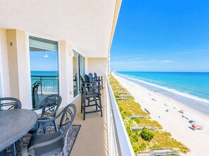 A balcony with a view of the beach, outdoor furniture, and a railing.