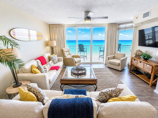 A living room with a view of the ocean, a ceiling fan, and a television.