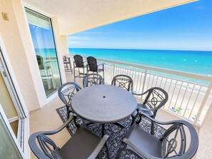 Ein Balkon mit Tisch und Stühlen mit Blick auf einen Strand und klares, blaues Wasser sowie Boote.