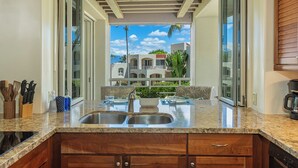 A kitchen with a double sink, wooden cabinets, and a view of a residential area.