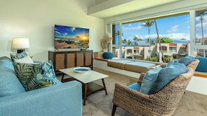 A living room with a sofa, a wicker chair, a table, and a painting of a sunset.