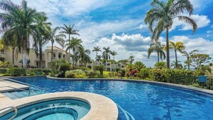 A swimming pool with a curved edge, surrounded by palm trees and a building with a tiled roof.