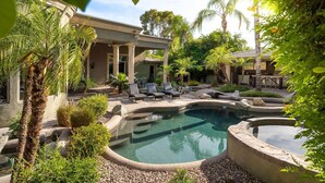 A pool area with lounge chairs, palm trees, and a building with columns.