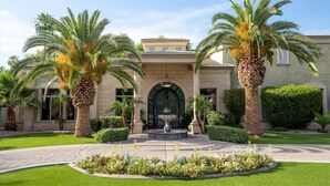 A building with a central entrance, palm trees, and a well-maintained garden.