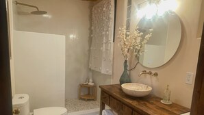 A bathroom with a wooden vanity, a round mirror, a toilet, and a shower area. - Charming Studio in lovely El Prado with AC (El Prado)