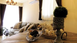 A living room with a sofa, a coffee table with decorative items, a chandelier, and an air conditioning unit. - MAISON DE AILE (Takasaki)