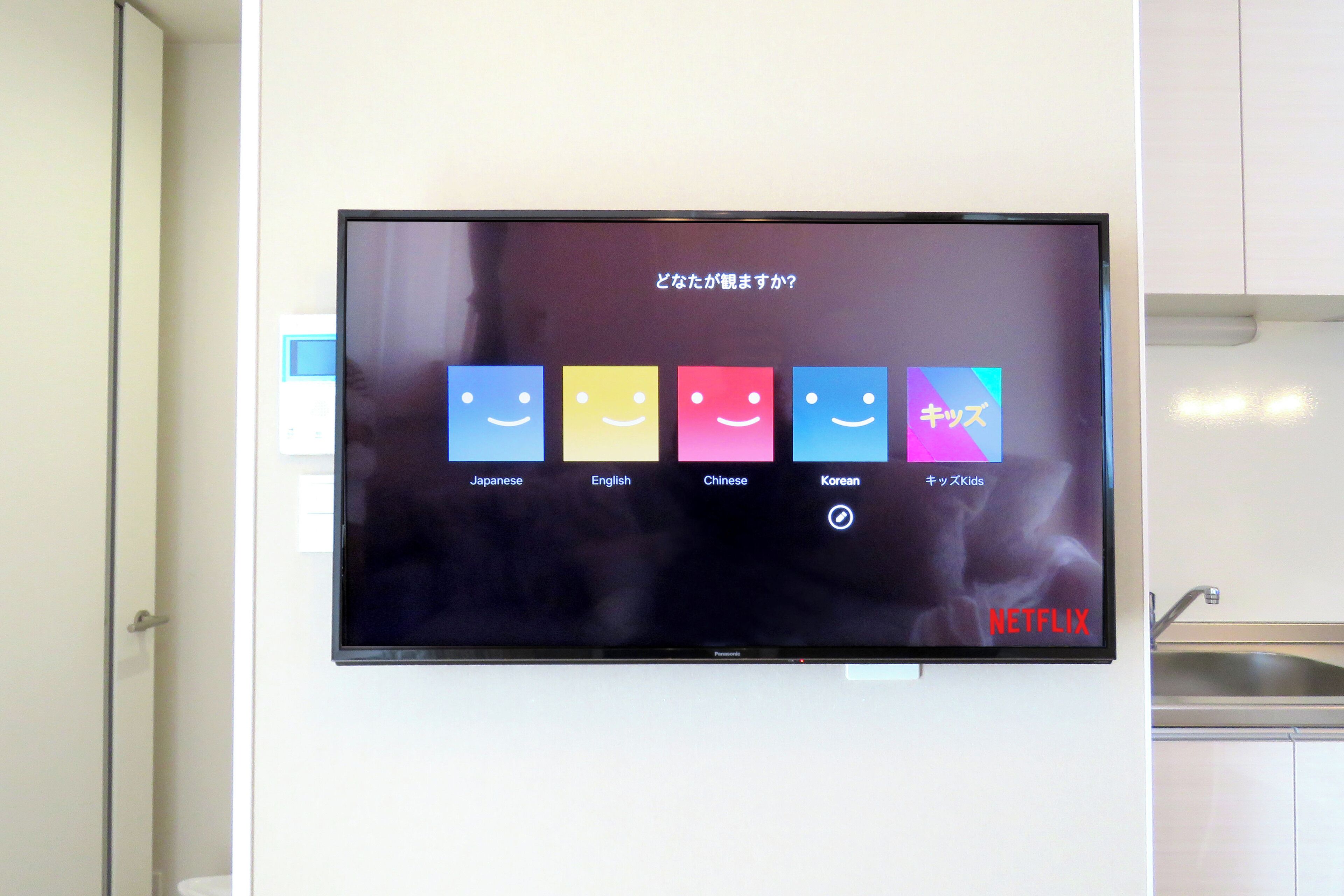 Un televisor montado en la pared mostrando una interfaz de selección de idioma con opciones para japonés, inglés, chino, coreano e infantil.