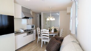 A compact living space with a kitchenette, dining area, and a sofa with cushions. - MAISON DE AILE (Takasaki)