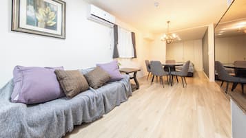 Een moderne woonkamer met een bank, een eettafel en stoelen. Er is een kroonluchter, een airconditioner en een ingelijst schilderij aan de muur.