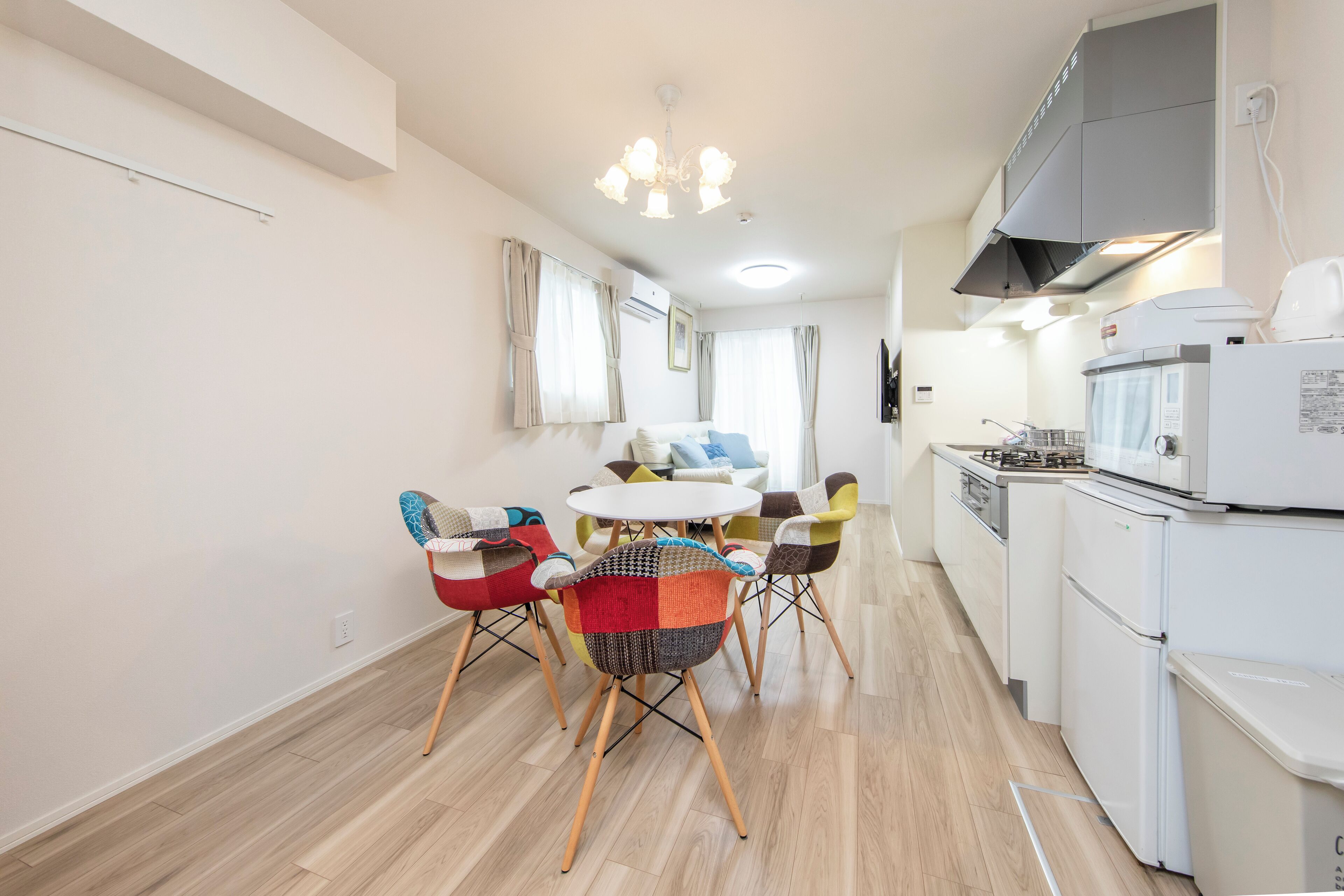 Una cucina moderna con zona pranzo, con frigorifero, piano cottura bianchi e un tavolo da pranzo con sedie colorate.