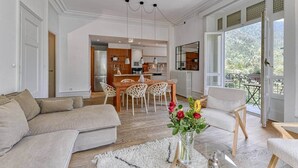 A modern living room with a sofa, chairs, a dining table, and a kitchen in the background. - Facing the Mont Blanc range. (Chamonix-Mont-Blanc)