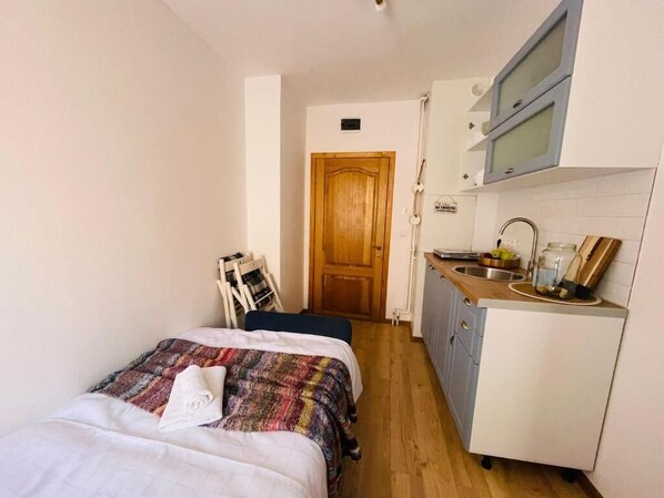 A compact room with a bed, a small kitchenette, and a wooden door.