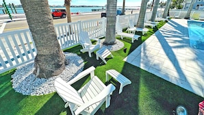 A poolside area with white Adirondack chairs, a small pool, and palm trees.