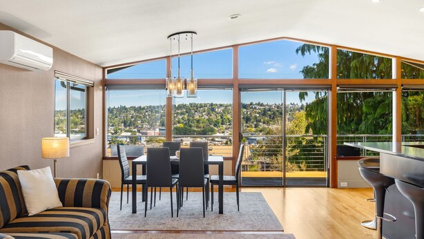 A modern living room with a dining area, large windows, and a view of a cityscape. - Queen Anne | Views | Near Shopping & Dining (Seattle)