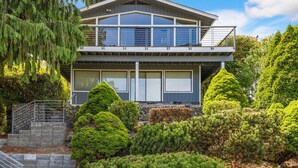 A modern two-story house with a balcony, surrounded by well-maintained greenery and a stone staircase. - Queen Anne | Views | Near Shopping & Dining (Seattle)