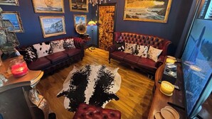 A room with dark blue walls, a chandelier, two red leather sofas with cowhide patterns, a wooden coffee table, and various framed artworks. - The Lobster Pot Scarbrough luxury Holiday Let (Scarborough)