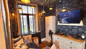 A cozy room with a bed, a dresser, a TV, and a window with blinds. - The Lobster Pot Scarbrough luxury Holiday Let (Scarborough)