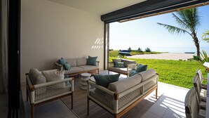 A modern living room with wicker furniture, a glass door leading to a balcony overlooking a beach. - CasaWapa - Waterfront Apartment (Pointe d'Esny)