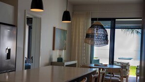 A modern kitchen with a central island, dining area with wicker chairs, and a large window with a view of the beach. - CasaWapa - Waterfront Apartment (Pointe d'Esny)
