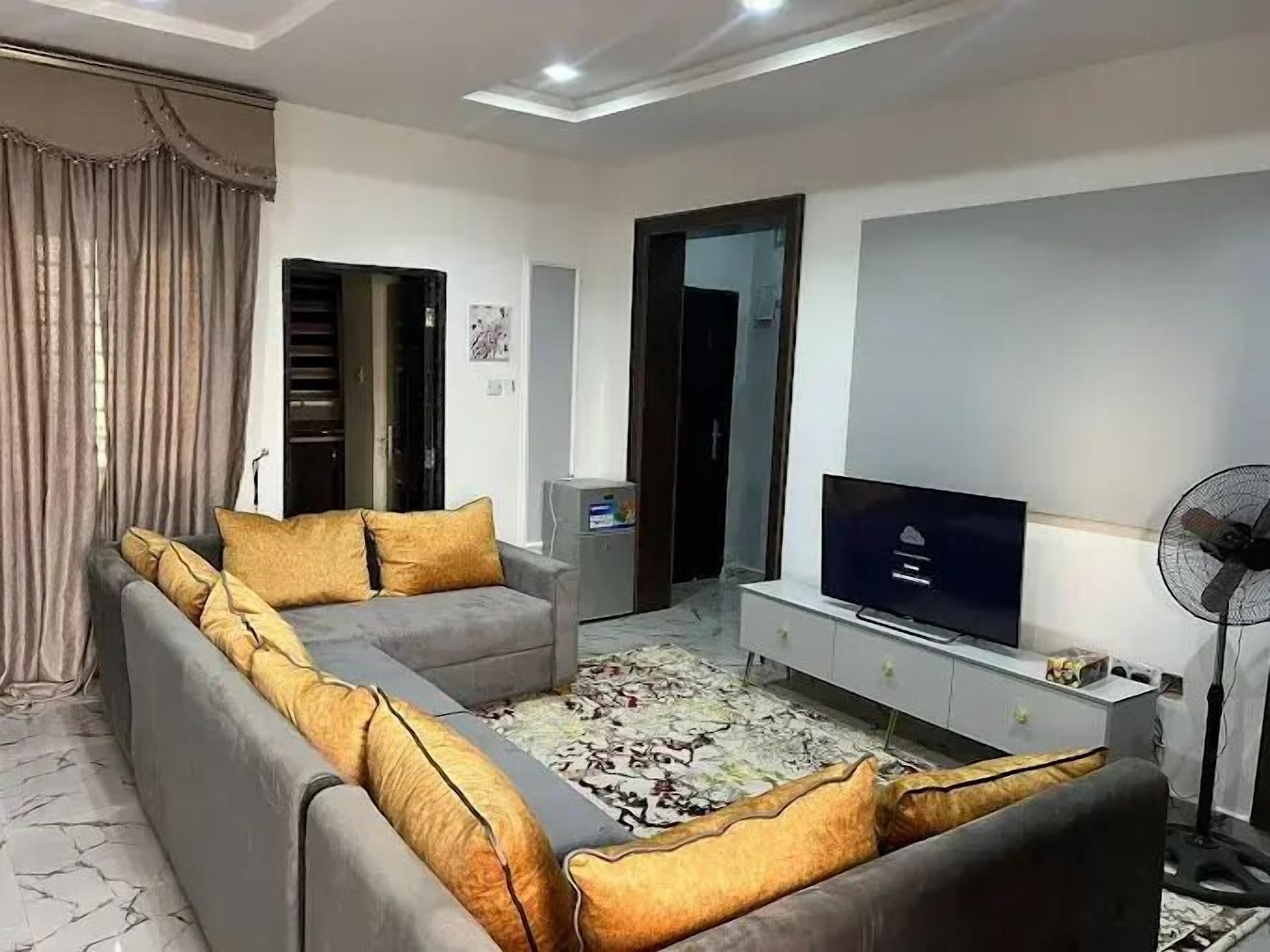 A modern living room with a grey sectional sofa, a flat-screen TV, a white entertainment unit, and a patterned rug.