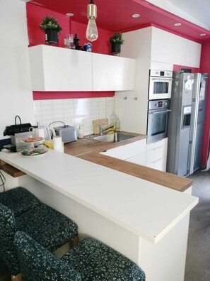 A modern kitchen with white cabinets, a central island, and a red accent wall.