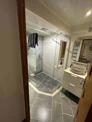 A modern bathroom with a glass-enclosed shower, a sink with a mirror, and tiled flooring.